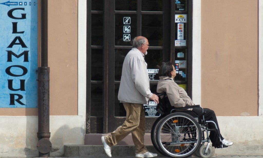 Man pushing woman in wheelchair passing business